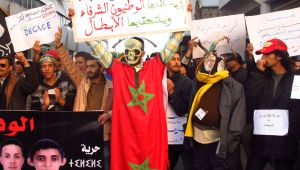 An activist wearing a skull mask and the flag of Morocco with a sign, saying the 'February 20th pro-democracy movement does not fear cowards and the corrupt' and is supported by the citizens, leads a demonstration in the capital Rabat Sunday, Feb. 19, 2019