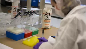 Image of a scientist in protective gear conducting biological research using micro pipettes and capillary tubes.