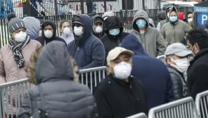 Patients wear personal protective equipment while maintaining social distancing as they wait in line for a COVID-19 test at Elmhurst Hospital Center, Wednesday, March 25, 2020, in New York.
