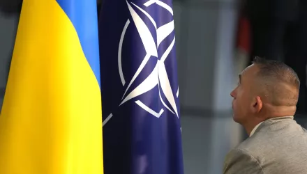 A man looks up at Ukraine and NATO flags side by side.