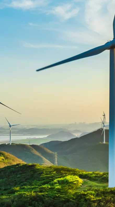 Wind turbines on a mountain ridge with the sea visible in the distance.