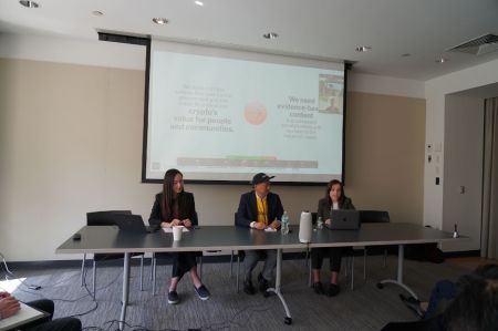 A group of three panelists at a table addressing a room of people